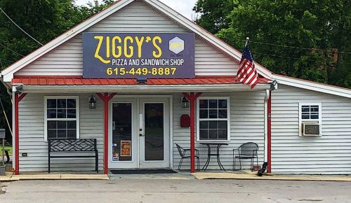 Exterior of Ziggy's Pizza and Sandwich Shop, featuring a sign, American flag, and outdoor seating area.