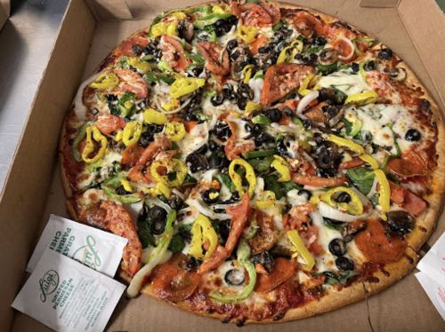 A large pizza topped with pepperoni, vegetables, olives, and cheese, in a pizza box with dipping sauces.