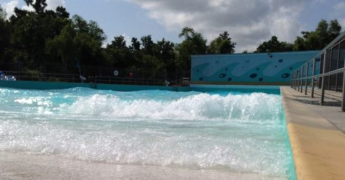 A wave pool with gentle waves, surrounded by trees and a colorful mural on the wall in the background.