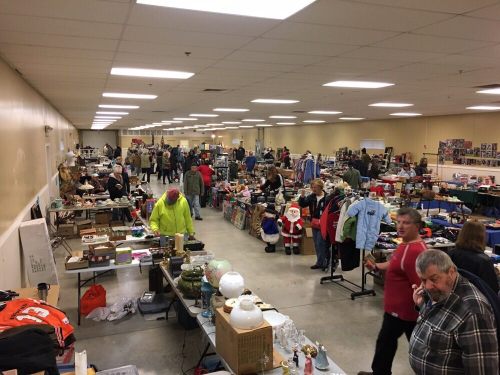 A bustling indoor market with vendors and shoppers browsing various items, including clothes and decorations.