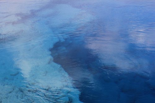 A serene view of clear blue water with gentle ripples, reflecting the sky above.