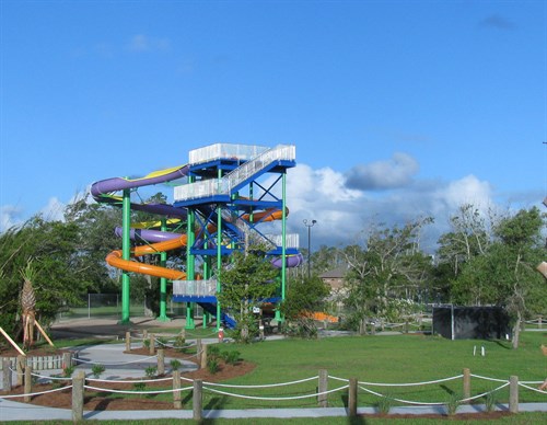 Colorful water slide structure with multiple twisting slides, surrounded by green grass and trees under a blue sky.