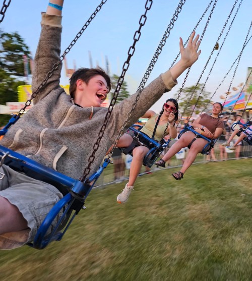 A group of friends joyfully swinging on a carnival ride, laughing and enjoying a sunny day at the fair.