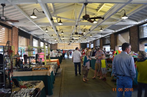 A bustling indoor market with vendors displaying crafts and jewelry, and visitors browsing the stalls.