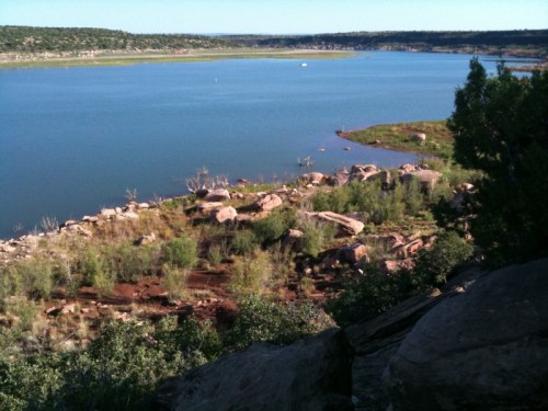 A serene lake surrounded by rocky shores and lush greenery under a clear blue sky.