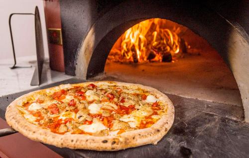 A freshly baked pizza with toppings, placed in front of a wood-fired oven with flames visible inside.
