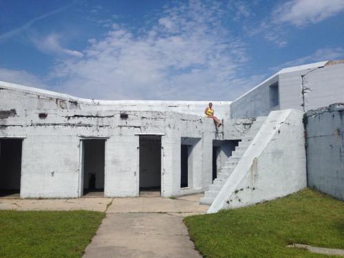 A person in a yellow shirt sits on a ledge of a weathered, white concrete structure with stairs and open doorways.