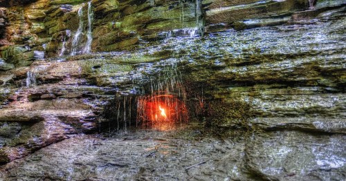 A small flame flickers in a rocky wall, surrounded by cascading water and textured stone.