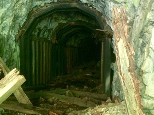 A dark, abandoned mine tunnel with wooden supports and debris scattered on the ground.