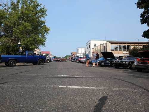 A street lined with classic cars and people, with trees and buildings in the background on a clear day.