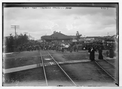 Crowd gathered at a train station in Fergus Falls, Minnesota, during Taft's visit, with people crossing the railroad tracks.