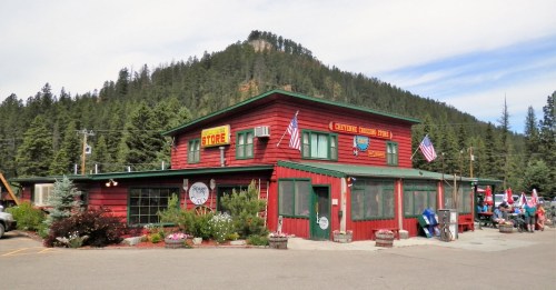 A red wooden store with flags, surrounded by trees and mountains, featuring a sign that reads "General Store."