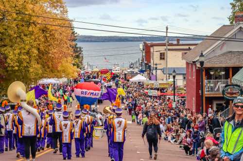 A lively parade with a marching band and colorful floats, surrounded by a large crowd and autumn foliage.