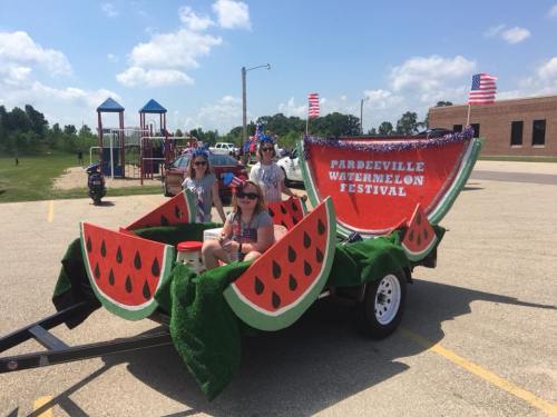 Three children sit on a decorated trailer shaped like a watermelon, promoting the Pardeeville Watermelon Festival.