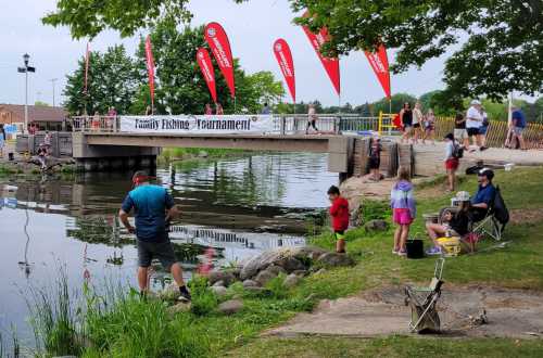 A family fishing tournament scene by a pond, with participants fishing and banners in the background.