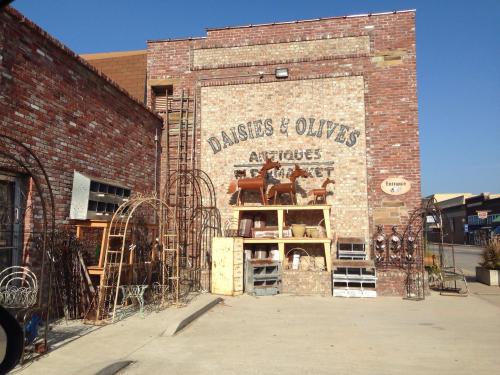 A brick building with "Daisies & Olives Antiques" sign, featuring outdoor displays of vintage furniture and decor.