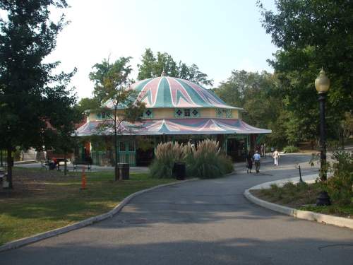A colorful, domed building surrounded by trees and pathways, with people walking nearby in a park setting.