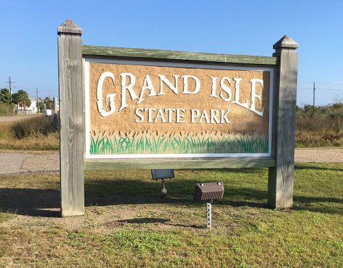 Sign for Grand Isle State Park, featuring large letters and a grassy design, set against a clear blue sky.