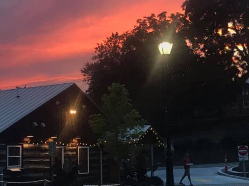 A cozy log cabin under a vibrant sunset, with a streetlamp illuminating the scene and trees in the background.