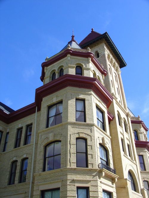 Historic building with a distinctive tower, featuring ornate brickwork and large windows against a clear blue sky.