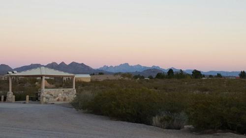 A serene landscape featuring distant mountains at sunset, with a gazebo and desert vegetation in the foreground.