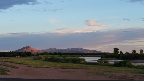 A serene landscape featuring a river, lush greenery, and mountains under a blue sky with soft clouds.