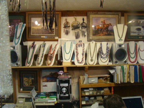 Display of colorful necklaces on stands, with framed art and decor in a shop setting.