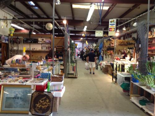 A bustling indoor market with various stalls, shoppers browsing, and colorful merchandise displayed along the aisles.