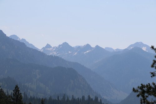 A panoramic view of misty mountains with snow-capped peaks and lush green valleys below.