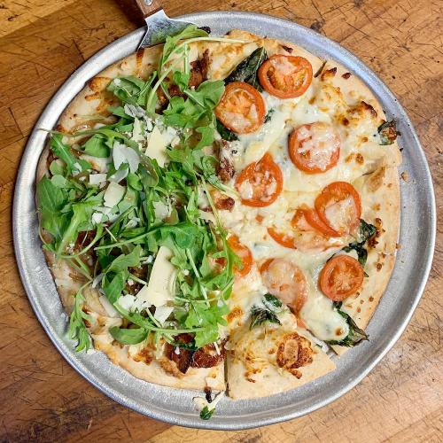 A pizza on a metal tray, half topped with tomatoes and cheese, half with fresh arugula and shaved cheese.