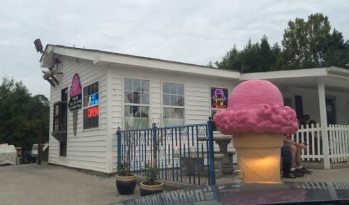 A quaint ice cream shop with a large pink ice cream cone sign and neon "Open" lights.