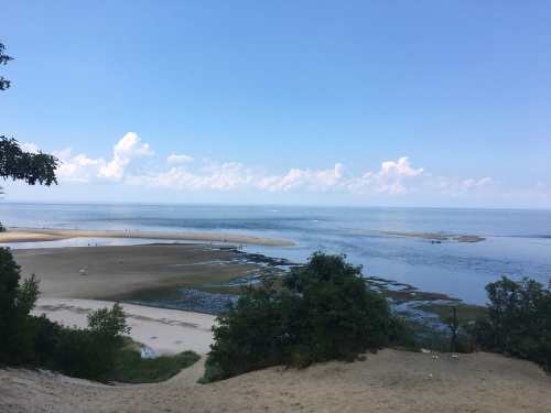 A serene beach scene with calm waters, sandy shores, and distant clouds under a clear blue sky.