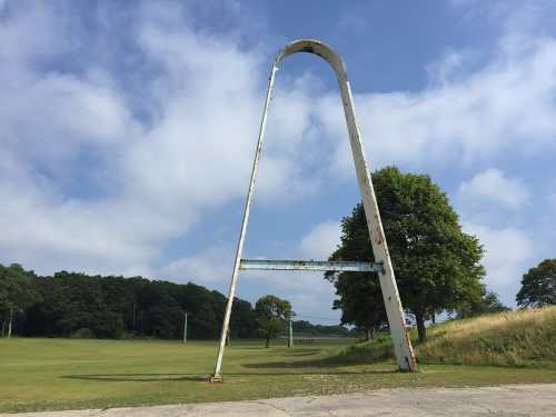 A large, weathered goalpost stands in a grassy field under a blue sky with scattered clouds.