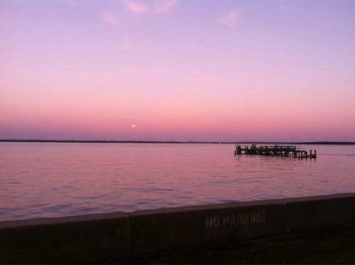 A serene sunset over a calm lake, with a silhouetted dock and soft pink and purple hues in the sky.