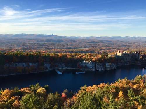 A scenic view of a river surrounded by vibrant autumn foliage and distant mountains under a clear blue sky.