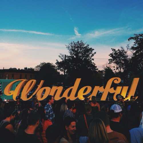 A crowd gathers in front of a large, colorful "Wonderful!" sign against a sunset sky.