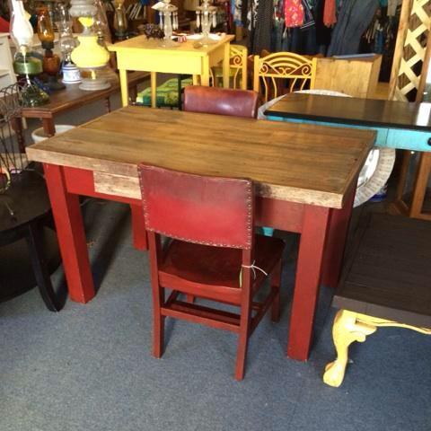 A rustic wooden table with a red base and a matching red chair, surrounded by various vintage furniture pieces.