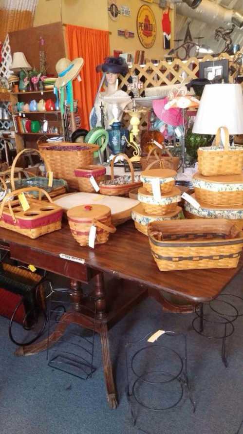 A table displays various woven baskets in different sizes and styles, surrounded by vintage decor in a shop.