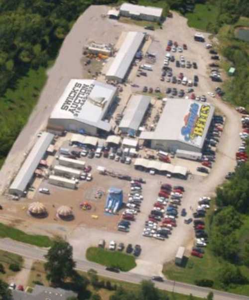 Aerial view of a large parking lot with several buildings and attractions, surrounded by greenery.