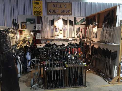 A cluttered golf shop filled with various golf clubs, bags, and accessories displayed on shelves and racks.