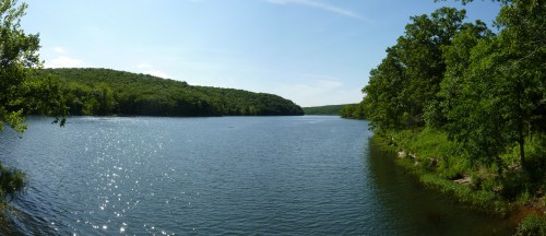 A serene river scene surrounded by lush green hills and trees under a clear blue sky.