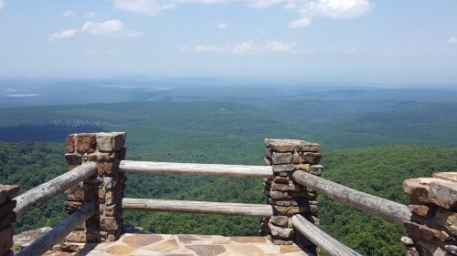 A scenic view from a stone overlook, showcasing lush green mountains and a clear blue sky in the distance.