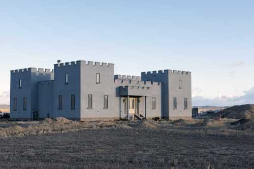 A large, castle-like building with a gray exterior and turreted roof, set in a barren landscape.