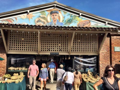 A bustling market entrance with a mural above, featuring a man and various baskets displayed outside.