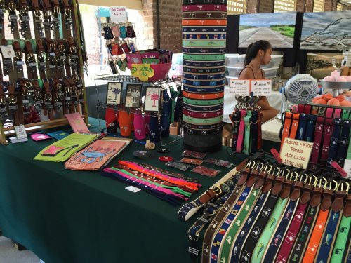A colorful display of various pet collars and accessories at a market stall, with a person browsing in the background.