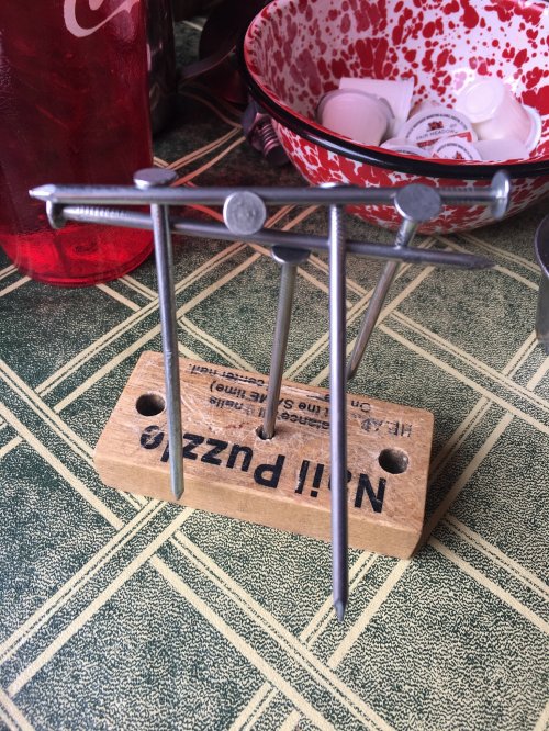 A wooden puzzle with three nails arranged in a triangular formation on a green tablecloth.