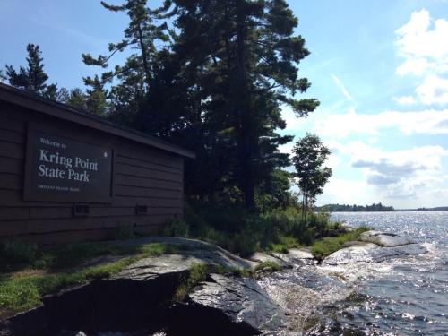 Sign for Kring Point State Park beside a rocky shoreline and shimmering water, surrounded by trees and a blue sky.
