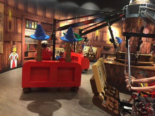 Children in a themed ride with wizard hats, surrounded by a whimsical, colorful interior resembling a magical library.