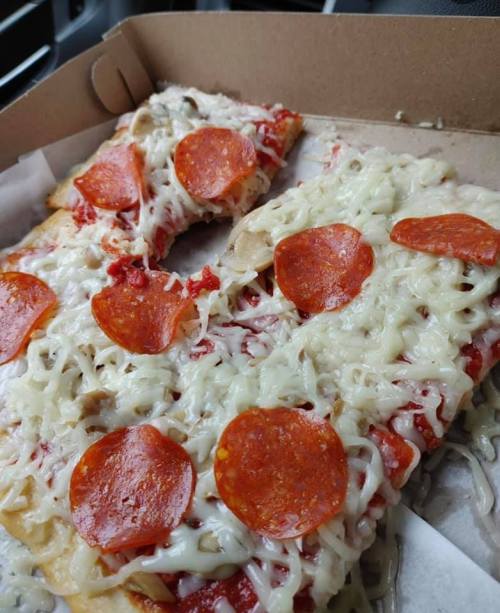 A close-up of a pepperoni pizza with melted cheese and mushrooms, partially eaten, in a takeout box.