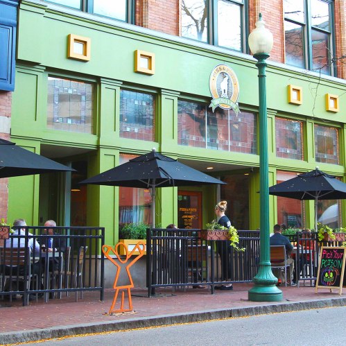 A vibrant restaurant exterior with outdoor seating, umbrellas, and a playful orange figure in front.